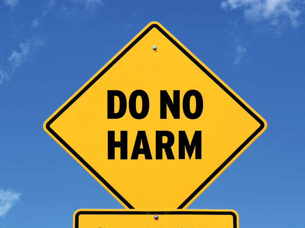 Caution sign against a blue sky with the words do no harm.